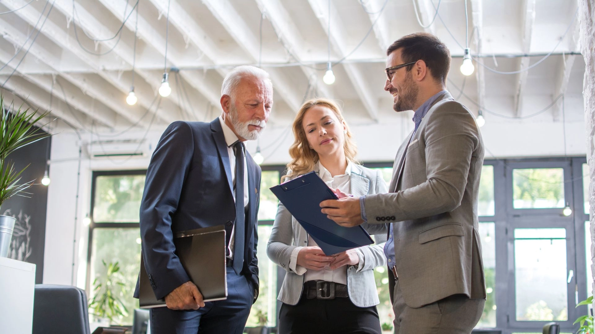 Drei Personen im Business-Outfit besprechen gemeinsam ein Dokument in einem modernen Büro.