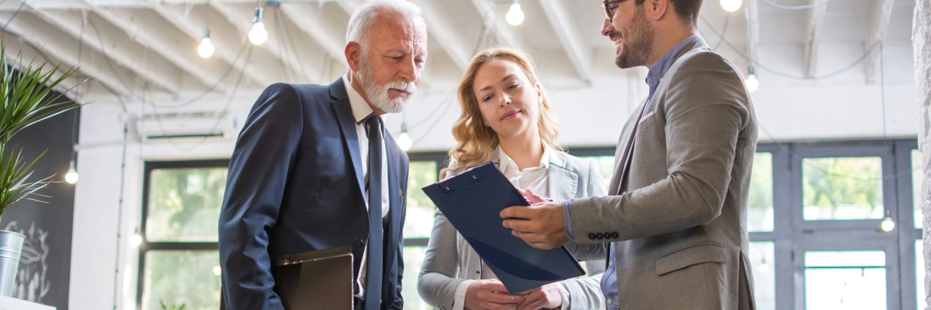 Drei Personen im Business-Outfit besprechen gemeinsam ein Dokument in einem modernen Büro.