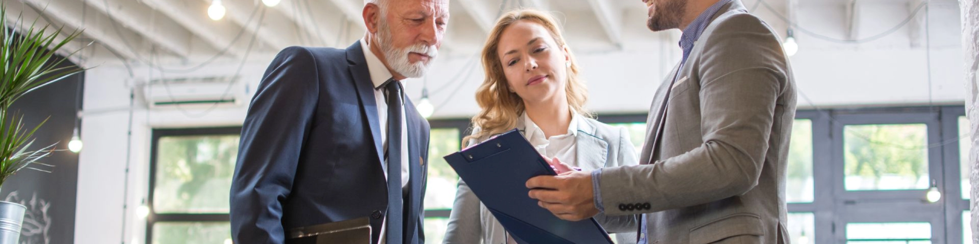 Drei Personen im Business-Outfit besprechen gemeinsam ein Dokument in einem modernen Büro.
