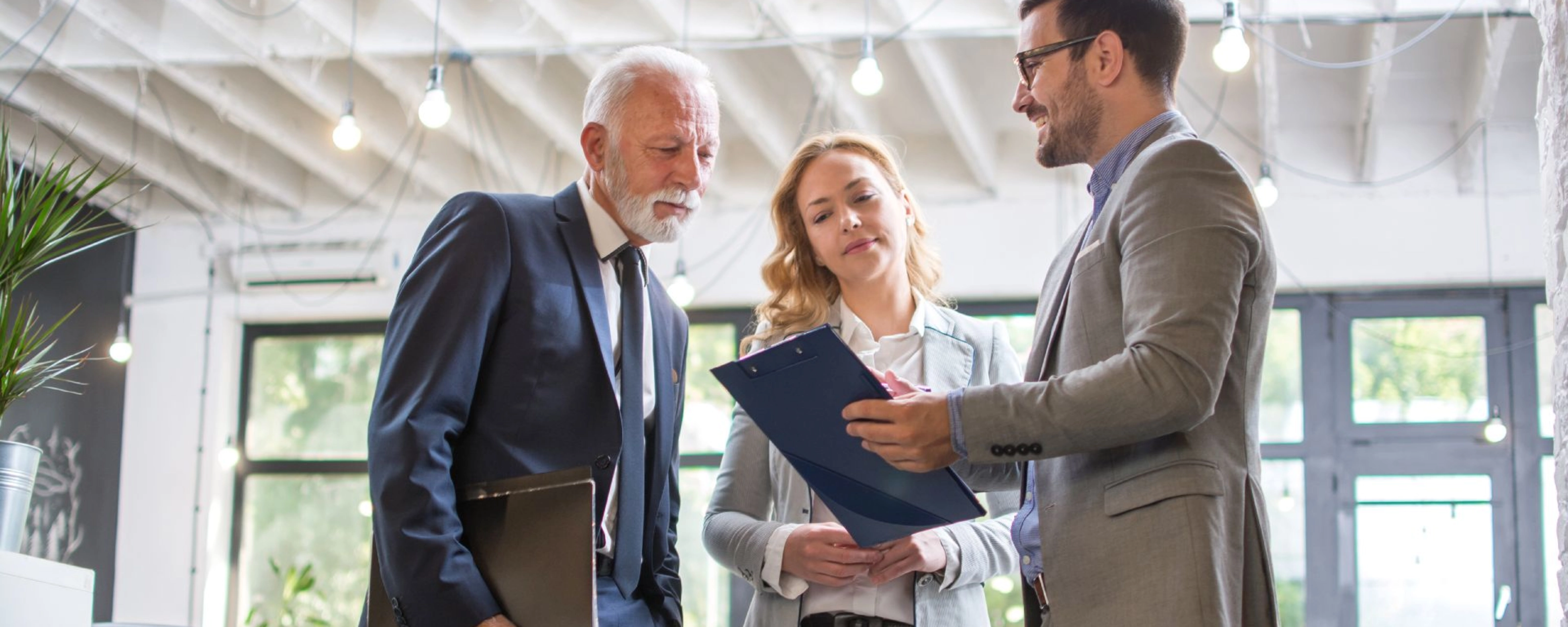 Drei Personen im Business-Outfit besprechen gemeinsam ein Dokument in einem modernen Büro.