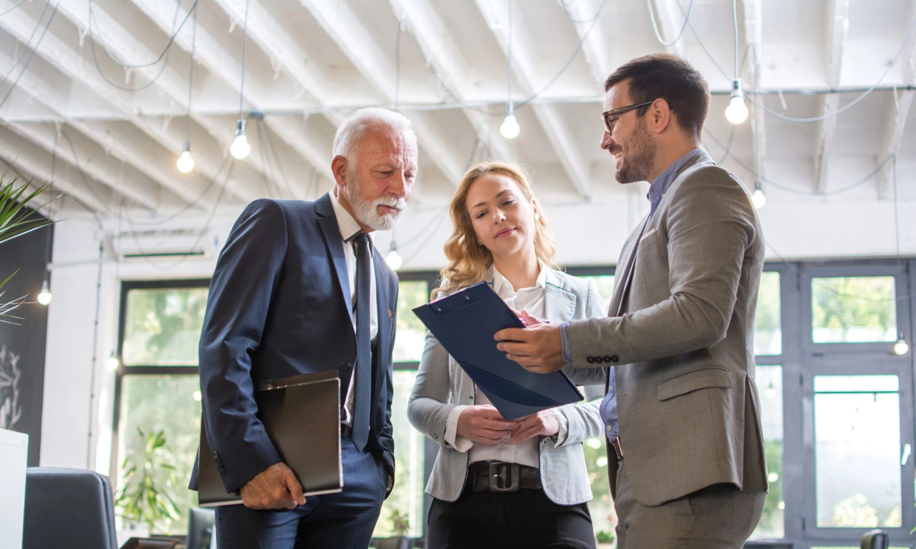 Drei Personen im Business-Outfit besprechen gemeinsam ein Dokument in einem modernen Büro.