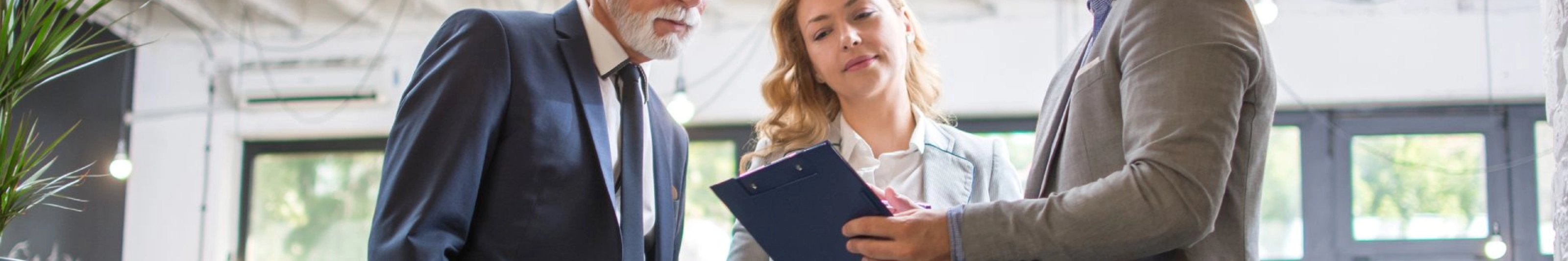 Drei Personen im Business-Outfit besprechen gemeinsam ein Dokument in einem modernen Büro.